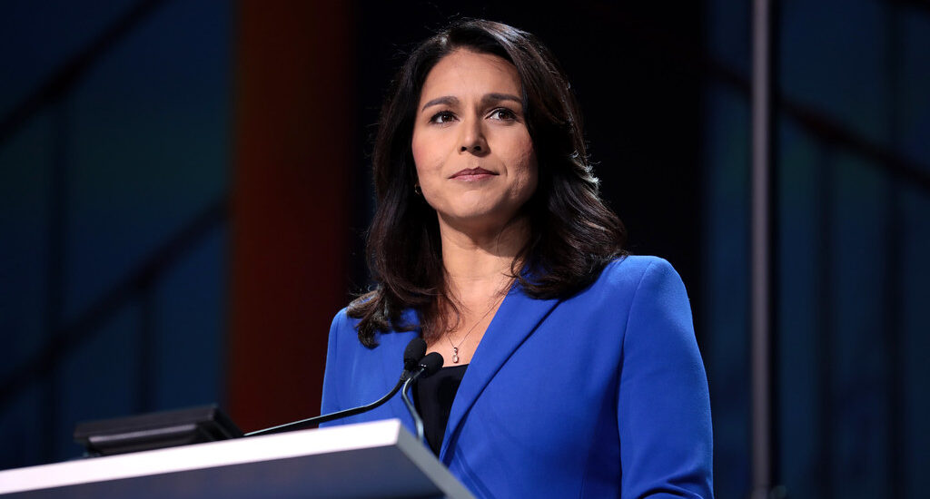 A woman in a blue suit stands confidently at a podium, addressing an audience with poise and professionalism.